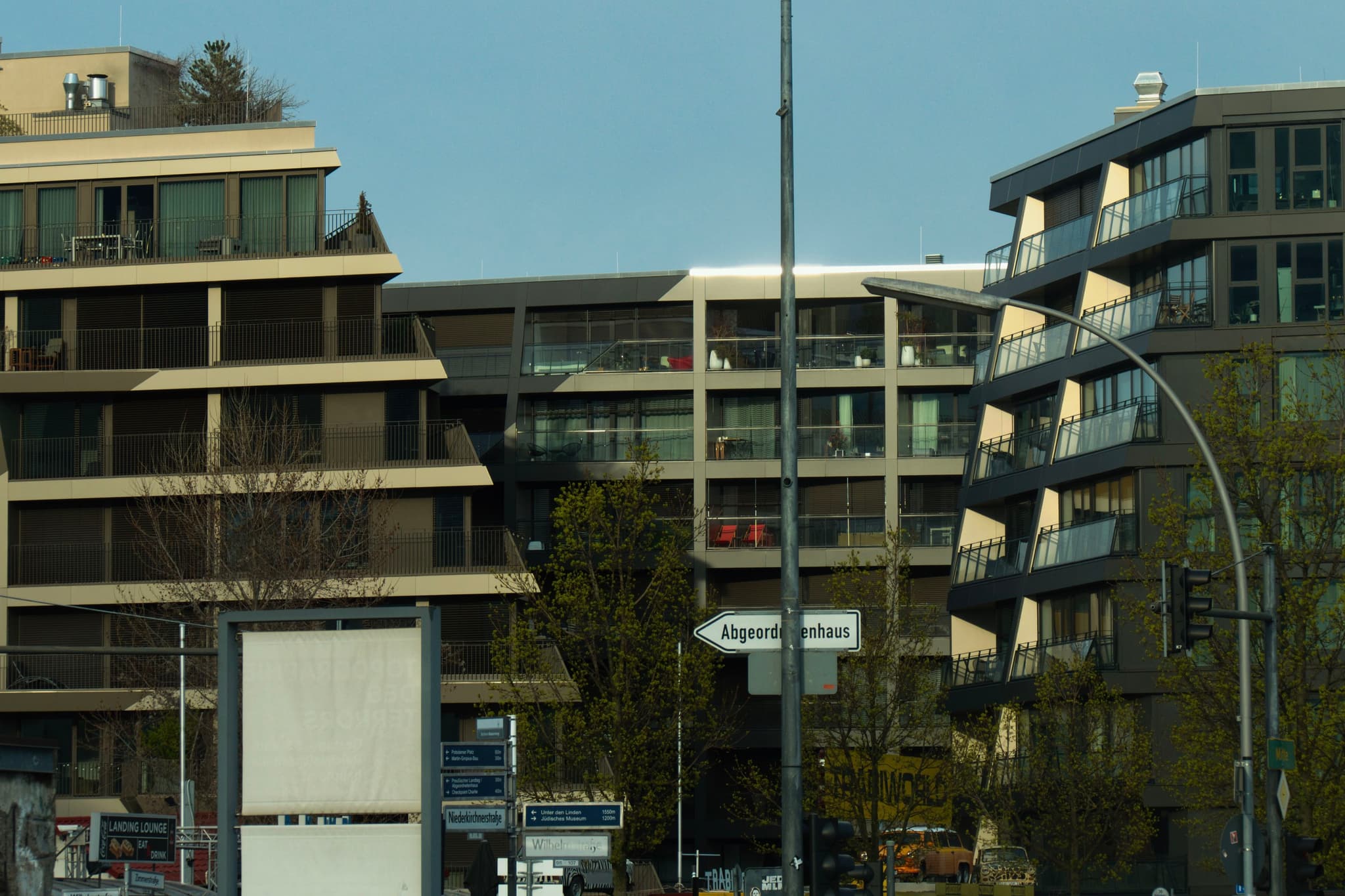 Modern multi-story buildings with large windows, surrounded by trees and street signs in the foreground