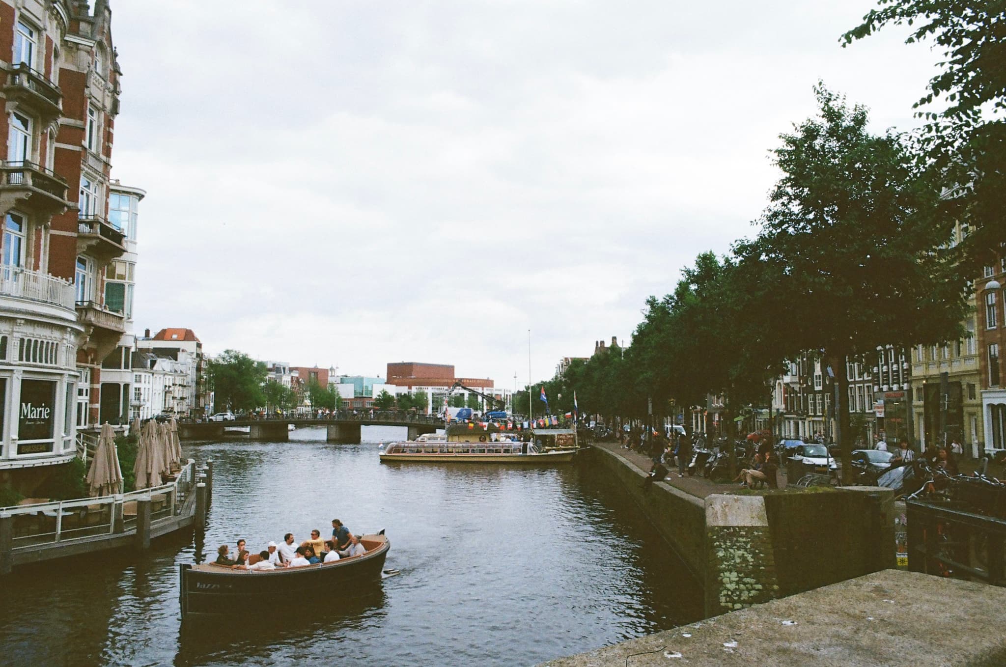 A canal scene with people in a boat, surrounded by buildings and trees, under a cloudy sky